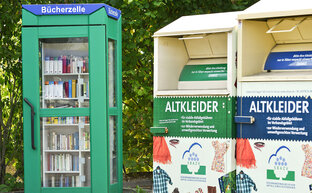Zwei Altkleidercontainer neben einer Bücherzelle