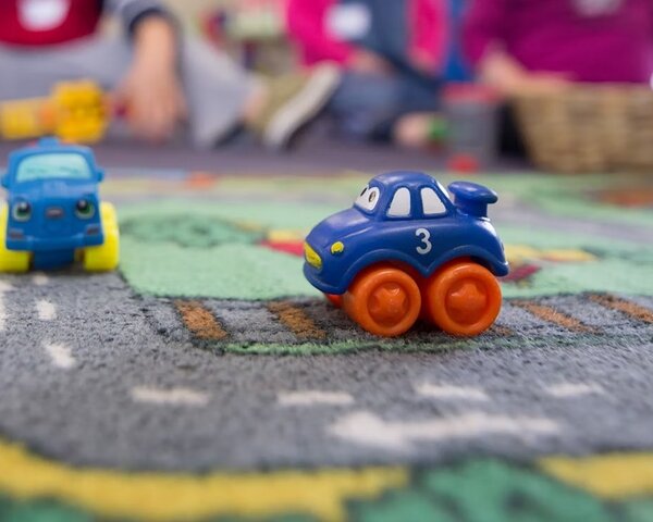 Kinder sitzen auf einem bunten Teppich im Spielzimmer und spielen mit kleinen Spielzeugautos.