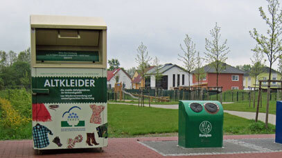 Ein Altkleidercontainer und zwei Glascontainer stehen in der Nähe einer Reihenhaussiedlung nebeneinander. 