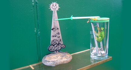 Eine gebastelte Wetterstation mit einem Plastikfrosch vor einem grünen Hintergrund.