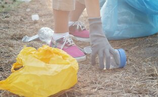 Eine Person sammelt Müll vom Boden. Auf dem Boden liegt eine gelbe Tüte