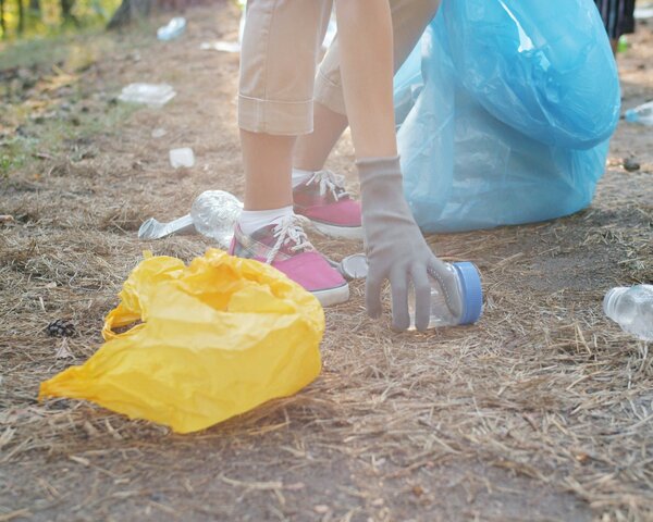 Eine Person sammelt Müll vom Boden. Auf dem Boden liegt eine gelbe Tüte