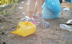 Eine Person sammelt Müll vom Boden. Auf dem Boden liegt eine gelbe Tüte