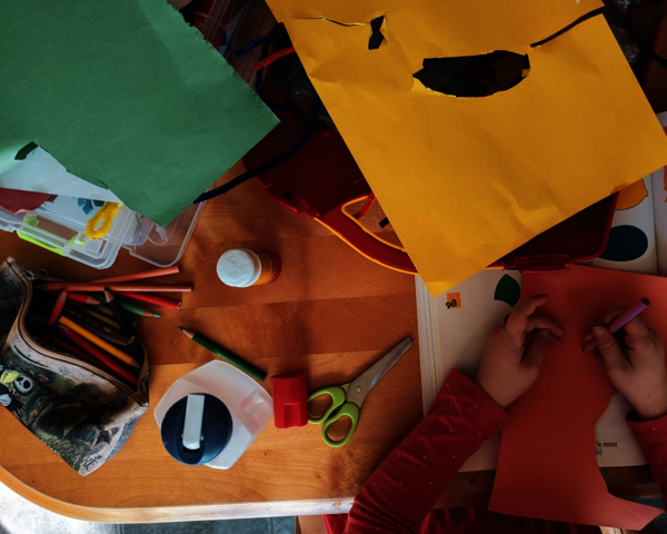 Ein Tisch von oben mit vielen unterschiedlichen Bastelmaterialien und den Händen eines Kindes, das etwas anmalt.