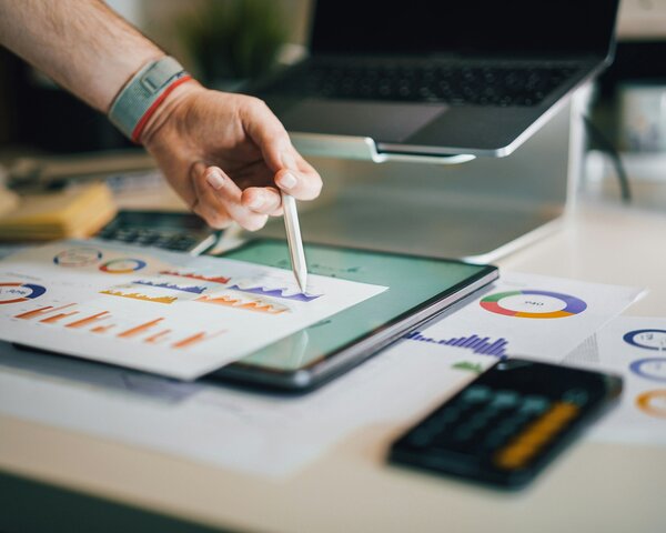 Eine Person tippt mit einem Stift auf einem Blatt Papier mit Statistiken. Das Blatt liegt auf einem Tablet mit weiteren Statistiken