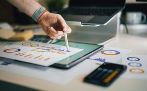 Eine Person tippt mit einem Stift auf einem Blatt Papier mit Statistiken. Das Blatt liegt auf einem Tablet mit weiteren Statistiken
