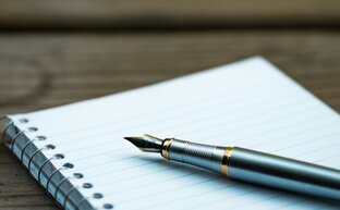 Ein Notizheft auf einem Holztisch, darauf liegt ein Füller.